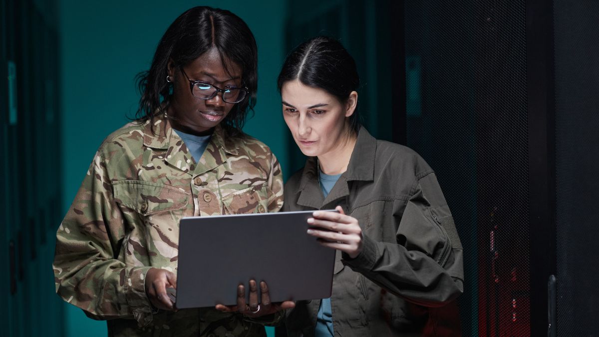 Two female military officers looking at a laptop in a server room